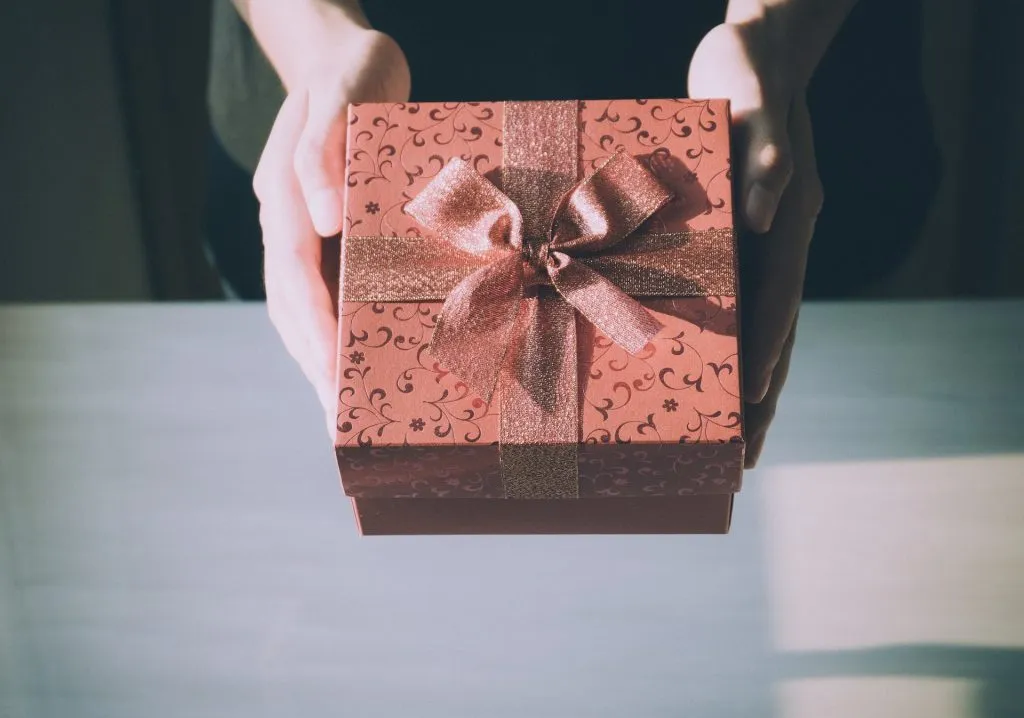 Hände überreichen ein rotes Geschenk mit Schleife als Belohnung für sicherheitsbewusstes Verhalten