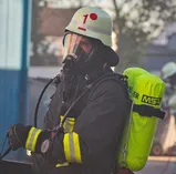 Feuerwehrmann mit Helm, Vollmaske und Pressluftatmer auf dem Rücken als Beispiel für Atemschutz