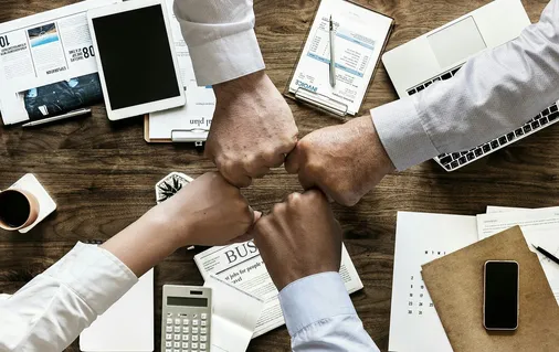 Vier Kollegen geben sich einen Faustgruß über dem Schreibtisch – gemeinsames Engagement im betrieblichen Gesundheitsmanagement