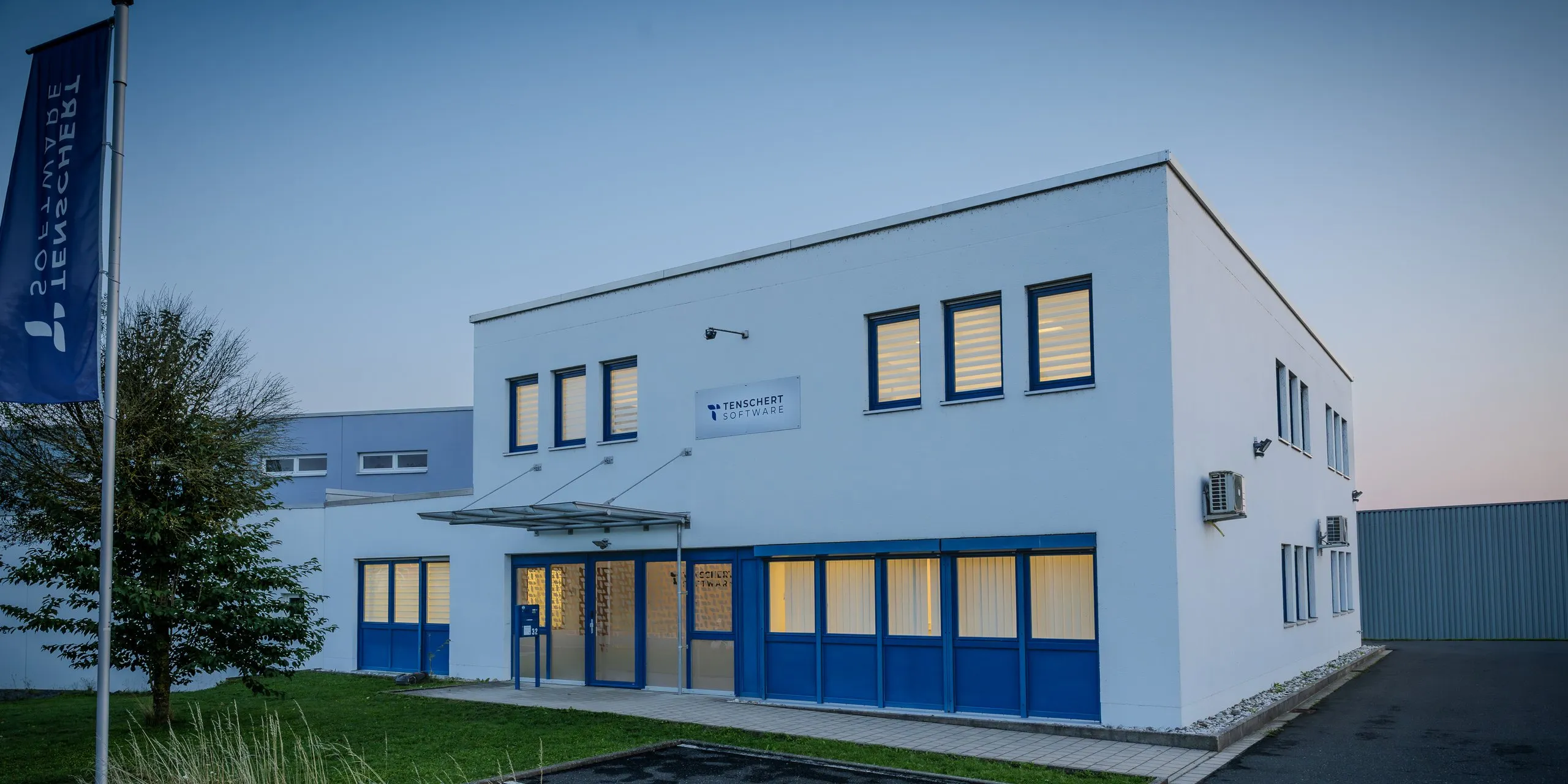 Zweigeschossiges weißes Bürogebäude der Tenschert Software GmbH in Berg b.Neumarkt i.d.OPf. mit Firmenfahne