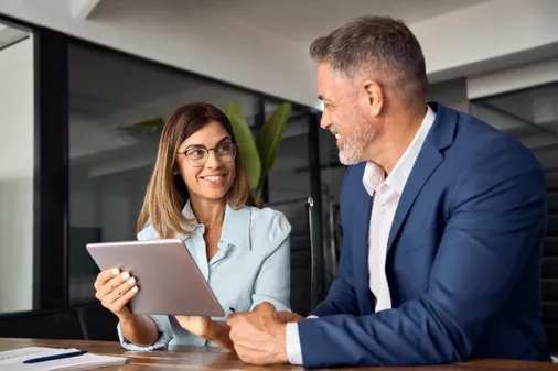 Zwei Führungskräfte besprechen sich lächelnd am Tablet im Büro – Weiterbildung durch Corporate Learning