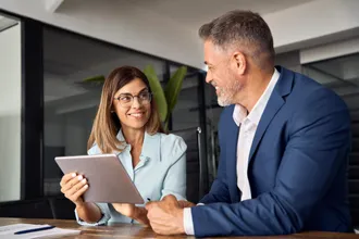 Zwei Führungskräfte besprechen sich lächelnd am Tablet im Büro – Weiterbildung durch Corporate Learning