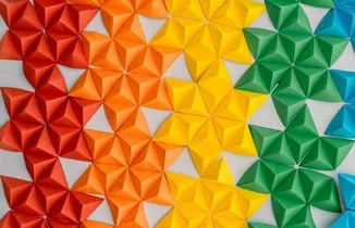 Bunte Papier-Origami-Sterne an einer Wand im Farbverlauf von Rot über Orange und Gelb zu Grün