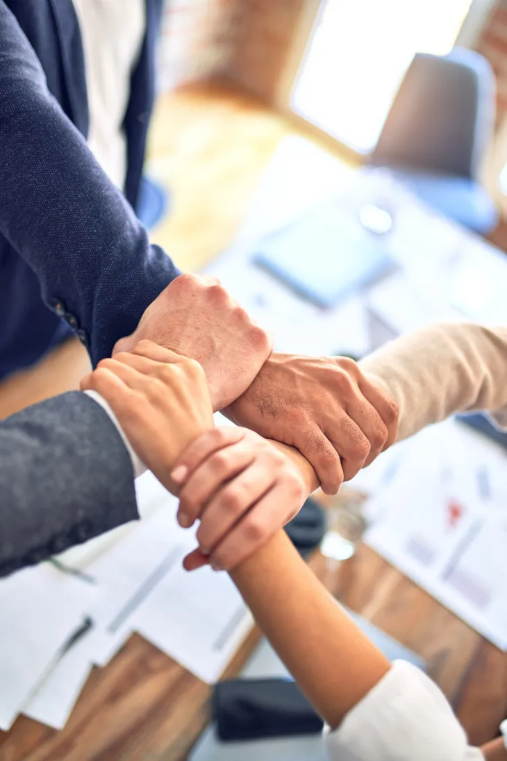 Vier Kollegen greifen sich im Büro an den Handgelenken – Teamwork als Basis für flexibles Lernen