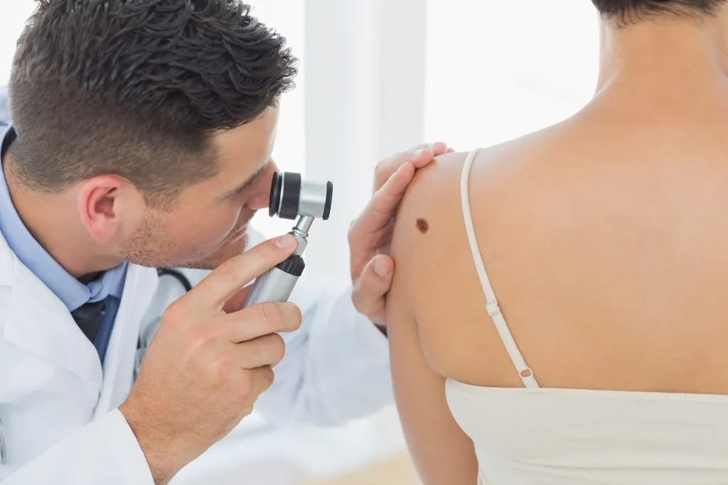 Hautarzt untersucht ein Muttermal auf der Schulter einer Patientin mit dem Dermatoskop zur Hautkrebs-Vorsorge