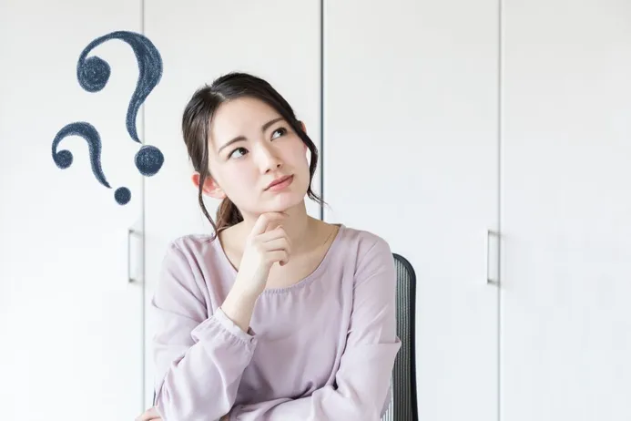 Nachdenkliche junge Frau blickt zu gezeichneten Fragezeichen an einer weißen Wand