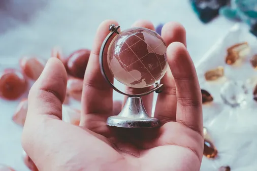 Hand hält einen kleinen Glasglobus als Symbol für mehrsprachige Unterweisungen in internationalen Teams