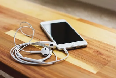 Smartphone mit angeschlossenen Kabel-Ohrhörern liegt auf einem Holztisch