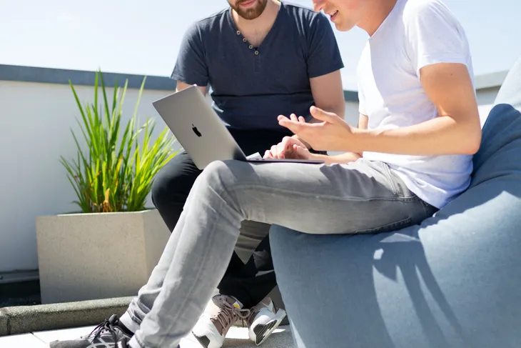 Zwei Kollegen sitzen draußen mit Laptop zusammen und besprechen die Einführung von Online-Schulungen