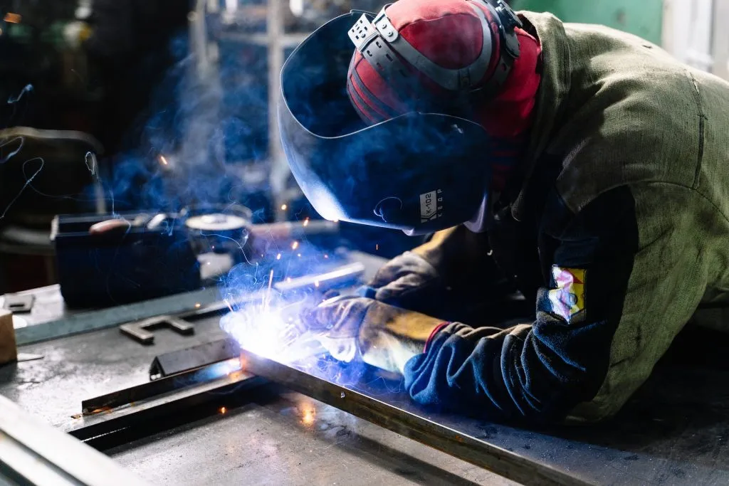 Schweißer mit Schutzmaske und Schutzhandschuhen schweißt Metall, Funken sprühen