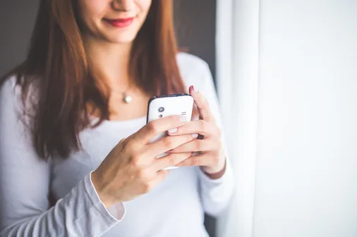 Lächelnde Frau bedient ihr Smartphone mit beiden Händen und nutzt eine mobilfreundliche Online-Schulung