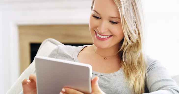 Lächelnde Frau erledigt ihre Online Unterweisung am Tablet auf dem Sofa