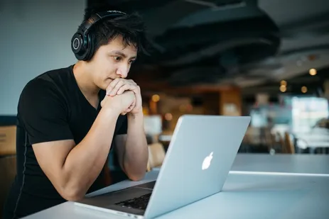 Junger Mann mit Kopfhörern lernt konzentriert am Laptop in einem Café