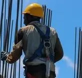 Bauarbeiter mit Schutzhelm und Auffanggurt arbeitet an Bewehrungsstäben eines Rohbaus