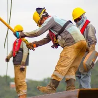 Bauarbeiter mit Schutzhelmen und roten Rettungswesten arbeiten auf Stahlträgern