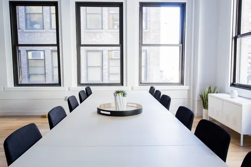 Heller Besprechungsraum mit langem Tisch, Stühlen und großen Fenstern zum richtigen Lüften im Büro