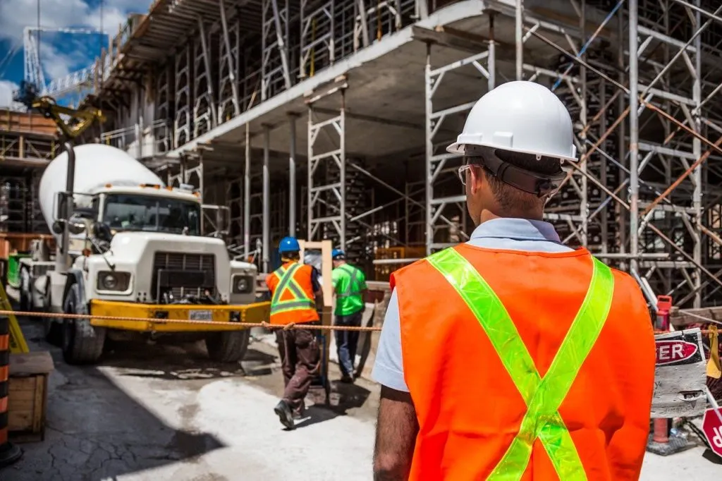 Bauarbeiter mit Helm und Warnweste blickt auf eine Baustelle mit Gerüst und Betonmischer