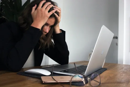 Verzweifelte Frau vergräbt vor ihrem Laptop die Hände im Haar